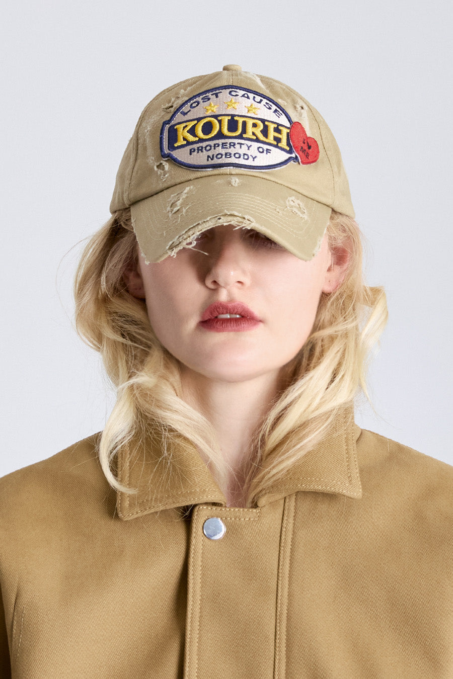 Person wearing a beige cap with branding and a matching jacket on a light gray background