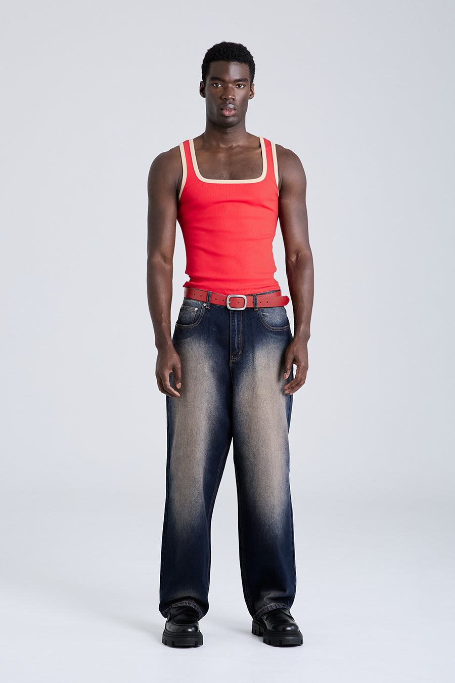 Man wearing a red tank top and dark jeans on a white background